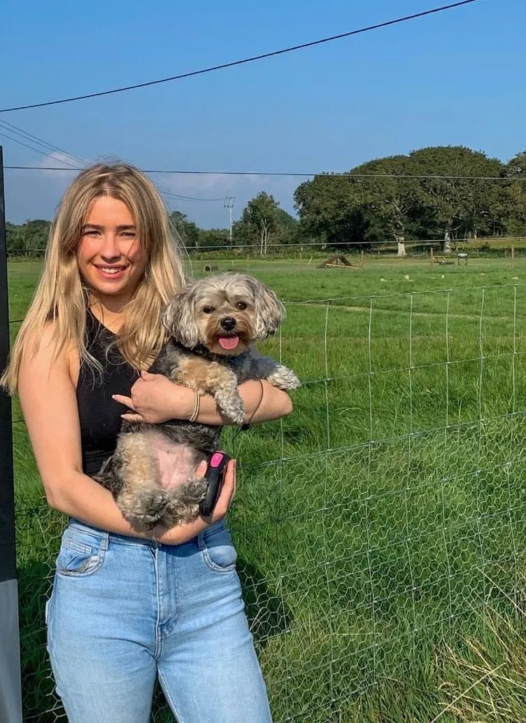 Kayla, the owner of Kay9 Grooming, holding a small dog in a field